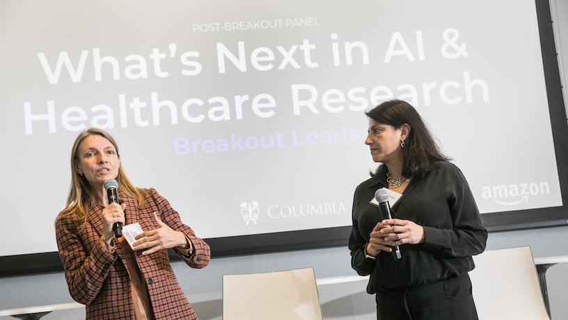 Two panelists holding microphones. Behind them, a screen reads "What's next in AI and Healthcare Research"