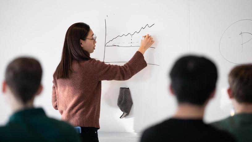 Someone demonstrating a line graph on a whiteboard. Attendees heads appear out of focus in the foreground.