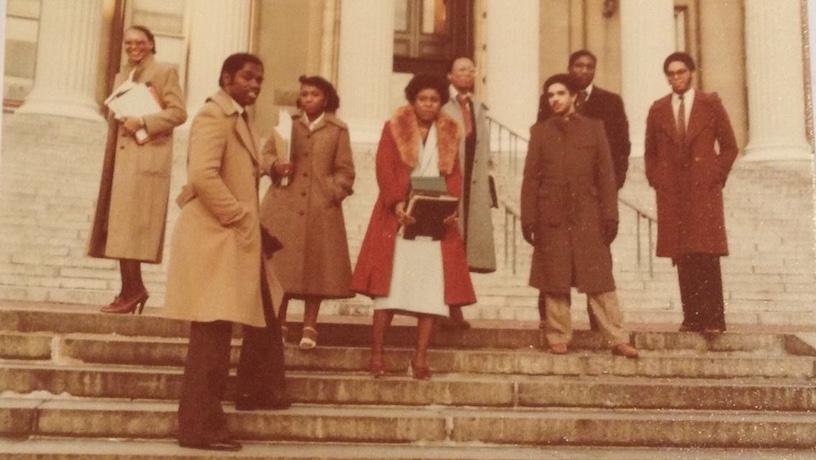 Eight people standing on the steps outside Columbia Low Library. In the background, the library pillars tower out of frame.