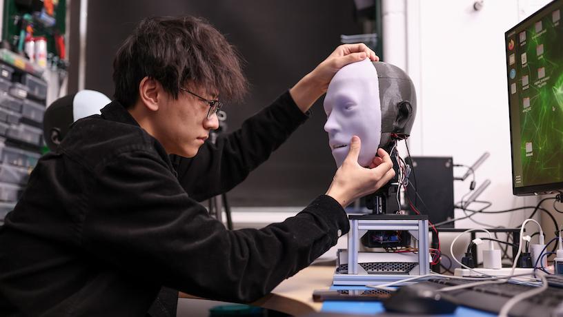 In their lab, a person adjusts the synthetic skin on a robotic face