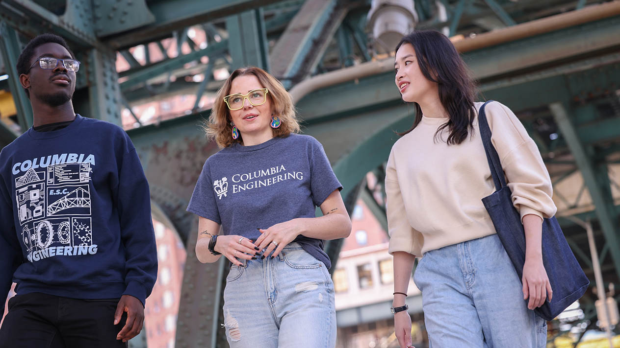 Three Columbia Engineering students walk under a large bridge in New York City.