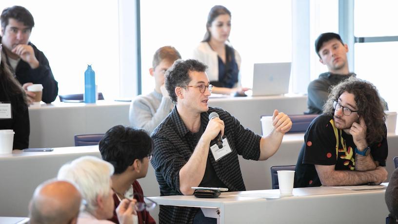 An attendee speaking into a microphone. Other attendees in the lecture hall look at them.