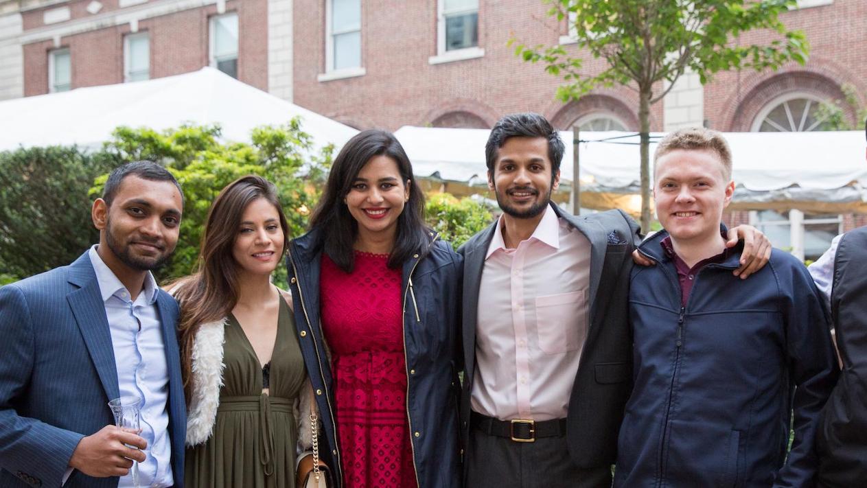 Five alumni smiling for a photo on Columbia University campus