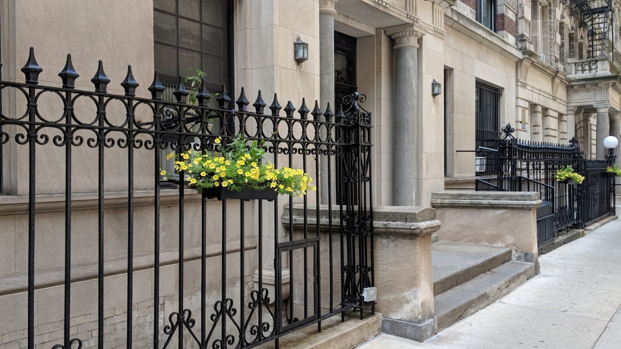 The ground floor of a building leads out onto a sidewalk. Flowers appear affixed to the gated exterior
