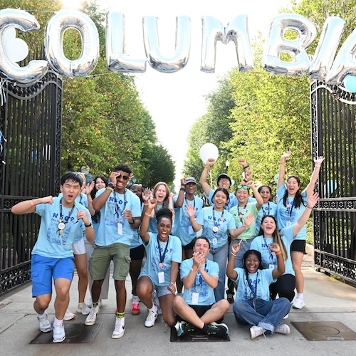 Columbia students wearing bright blue shirts cheering in front of the campus gates