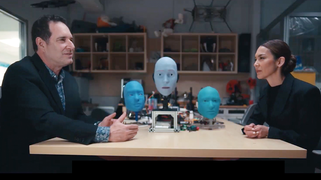 Hod Lipson in an interview with a Bloomberg reporter. Robot faces are seen on the table in between them