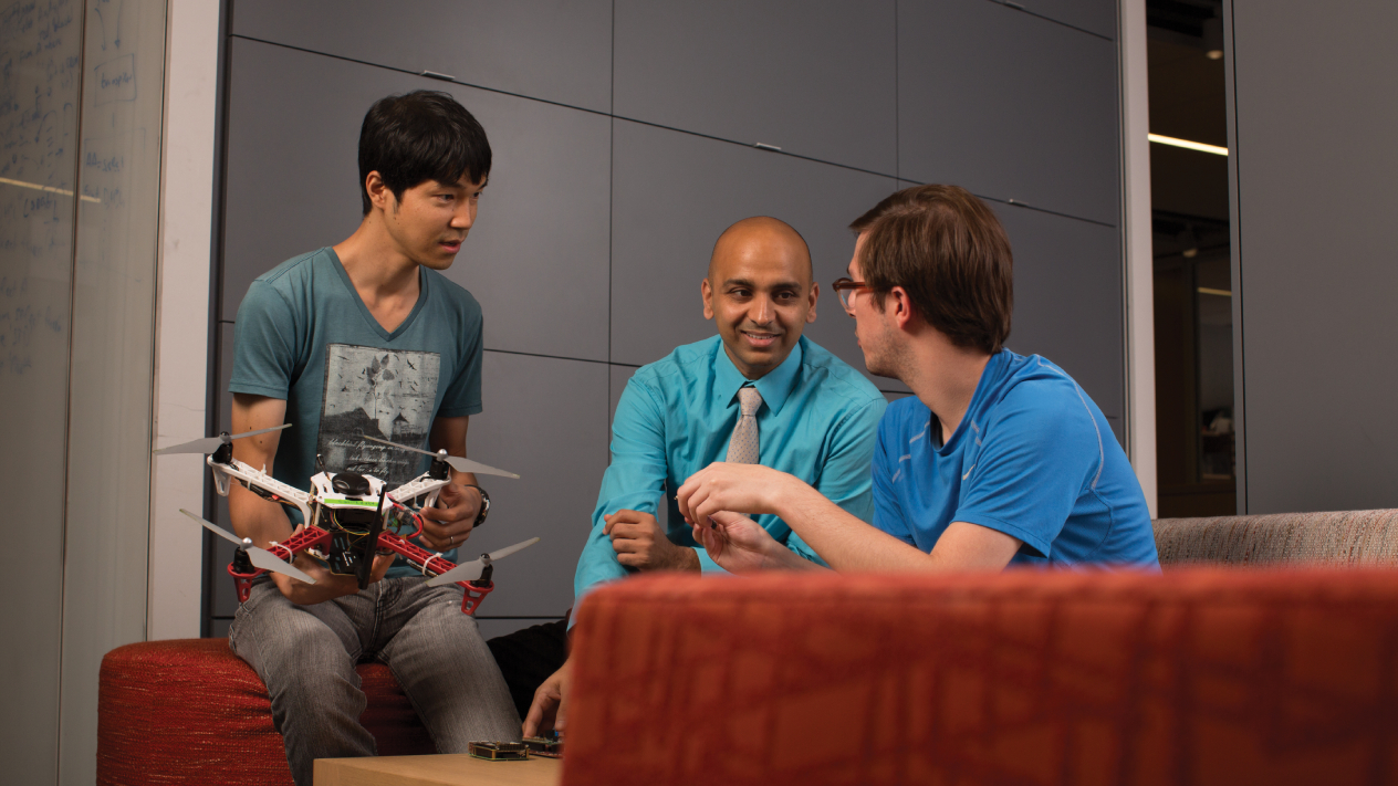 Simha Sethumadhavan with two students. The student on the left holds a quadrotor drone