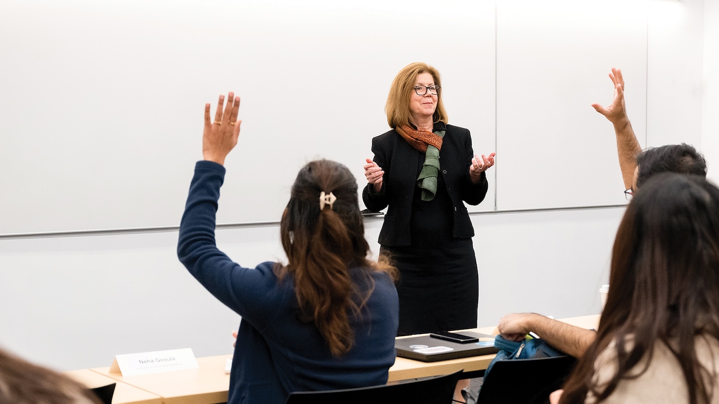 Georgia Papathomas standing in front of a room of students raising their hands