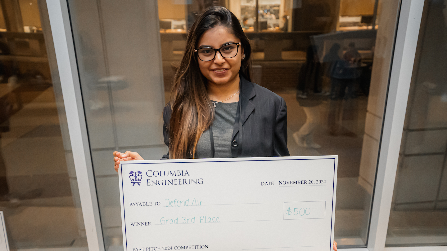 A student holding up a giant $500 check payable to DefendAir