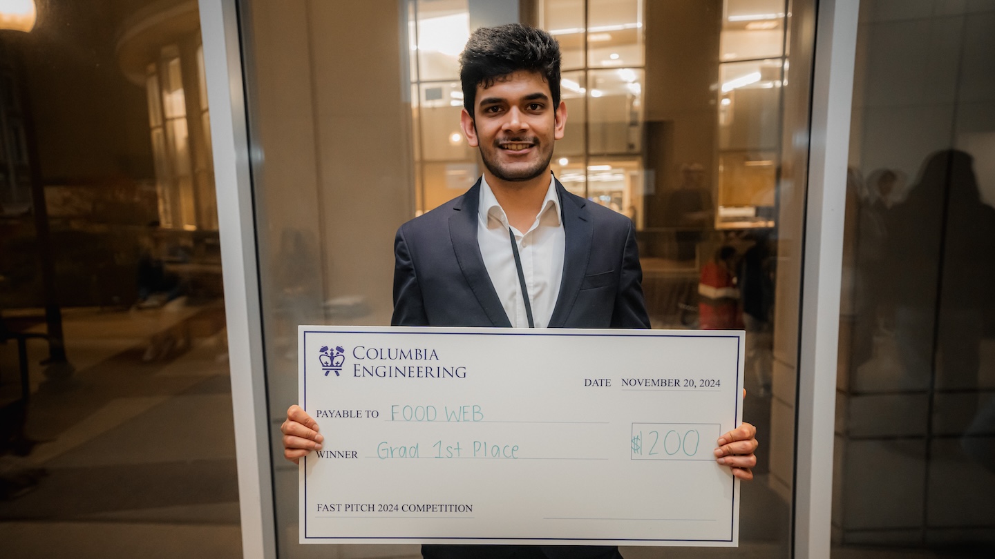 A student holding up a giant $1,200 check payable to Food Web