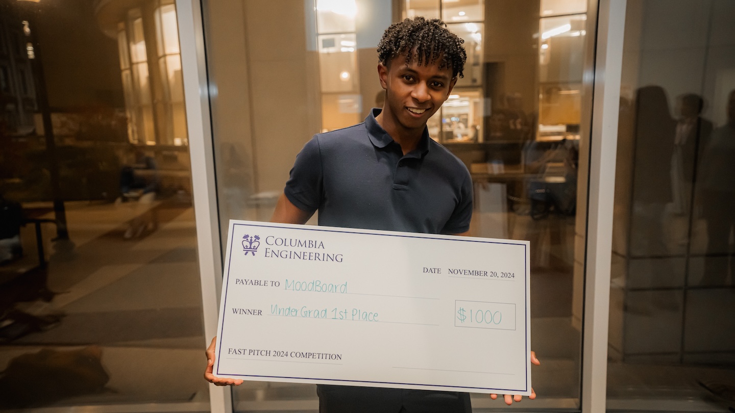 A student holding up a giant check for $1000, payable to MoodBoard