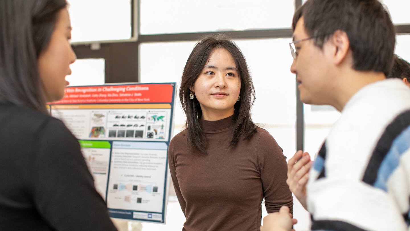 Three Columbia AI Summit attendees conversing next a research display board