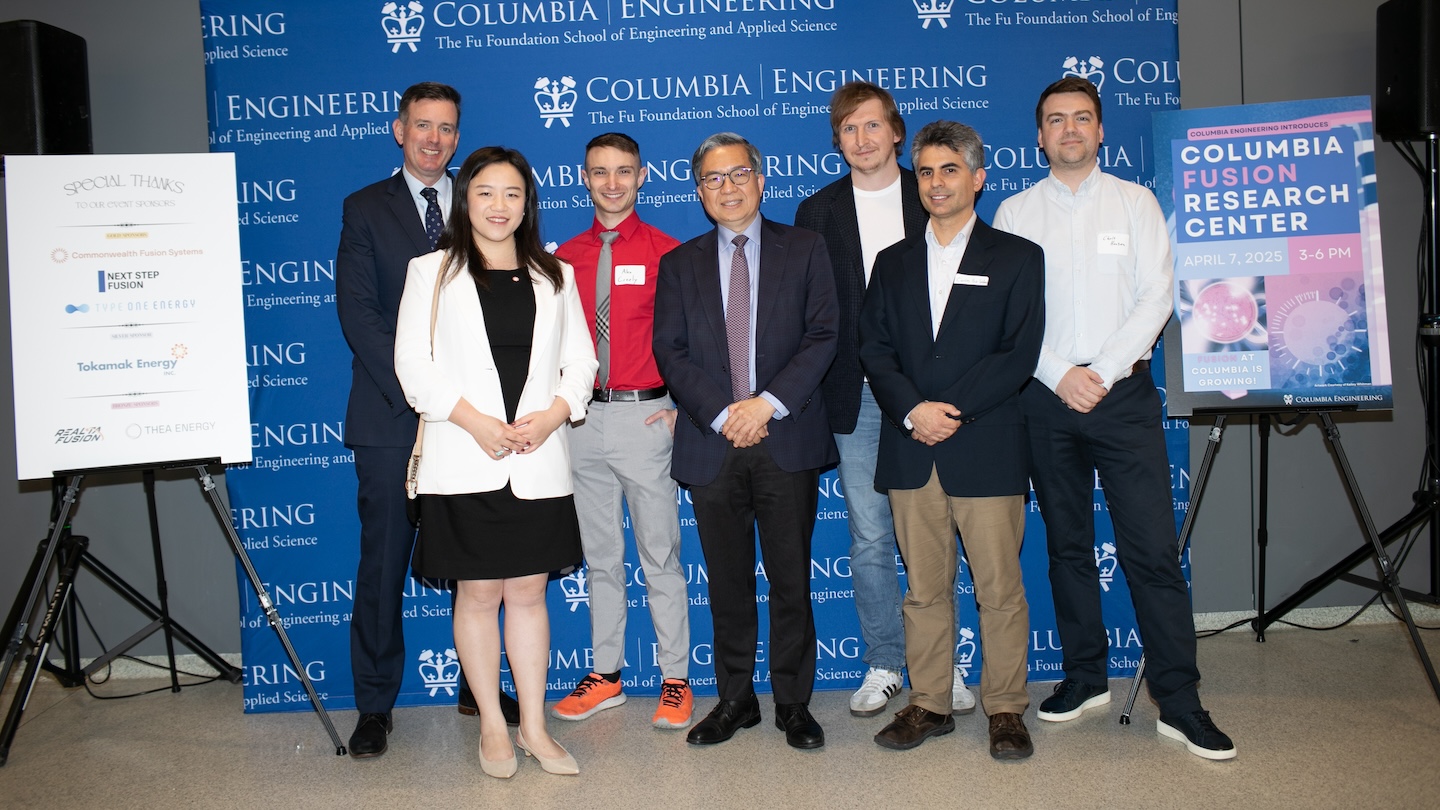 Seven people posing for a photo in front of a Columbia Engineering-themed backdrop. Two posters flank the group. The one on the right reads "Columbia Fusion Research Center"