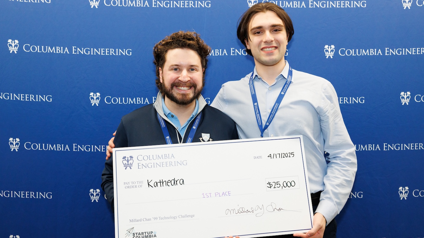 Two people smiling and holding a giant, $25,000 check addressed to Kathedra