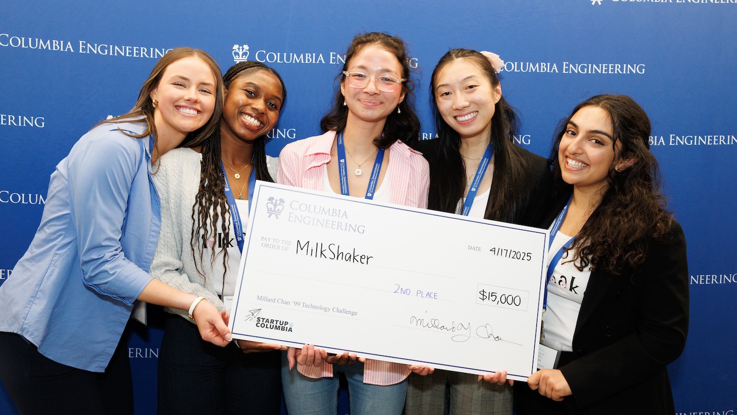 Five women smiling and holding a giant, $15,000 check addressed to Milkshaker