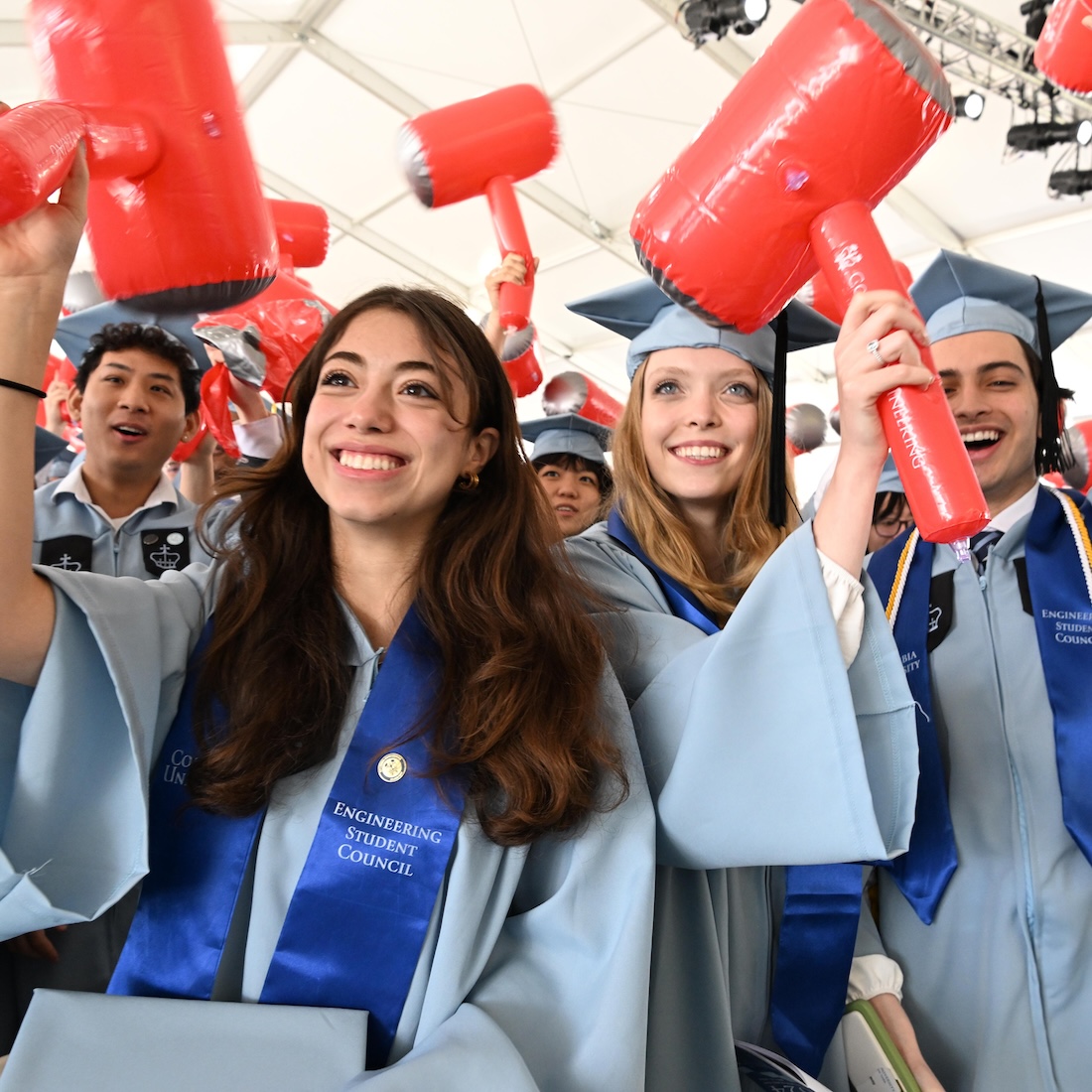 Columbia Engineering students in graduation regalia smiling and holding inflatable red hammers