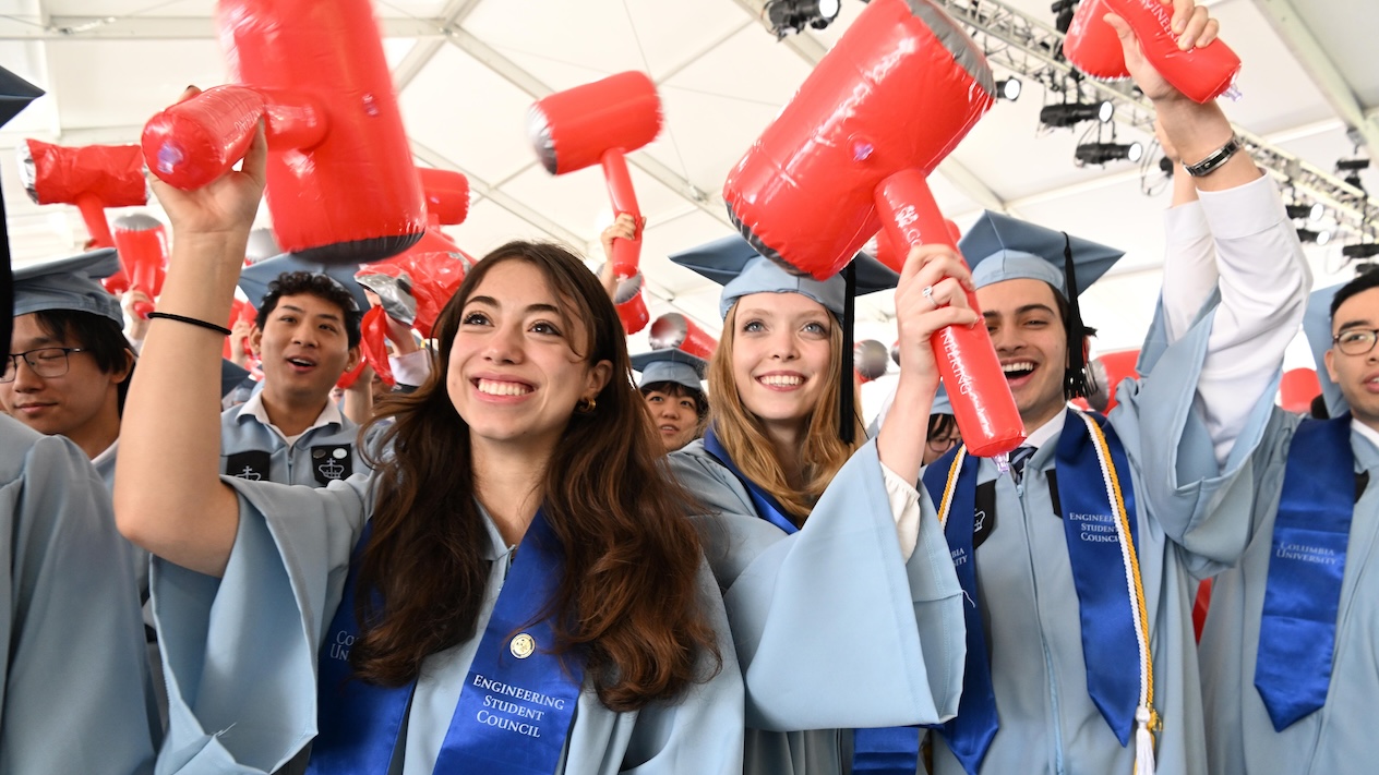 Columbia Engineering students in graduation regalia smiling and holding inflatable red hammers
