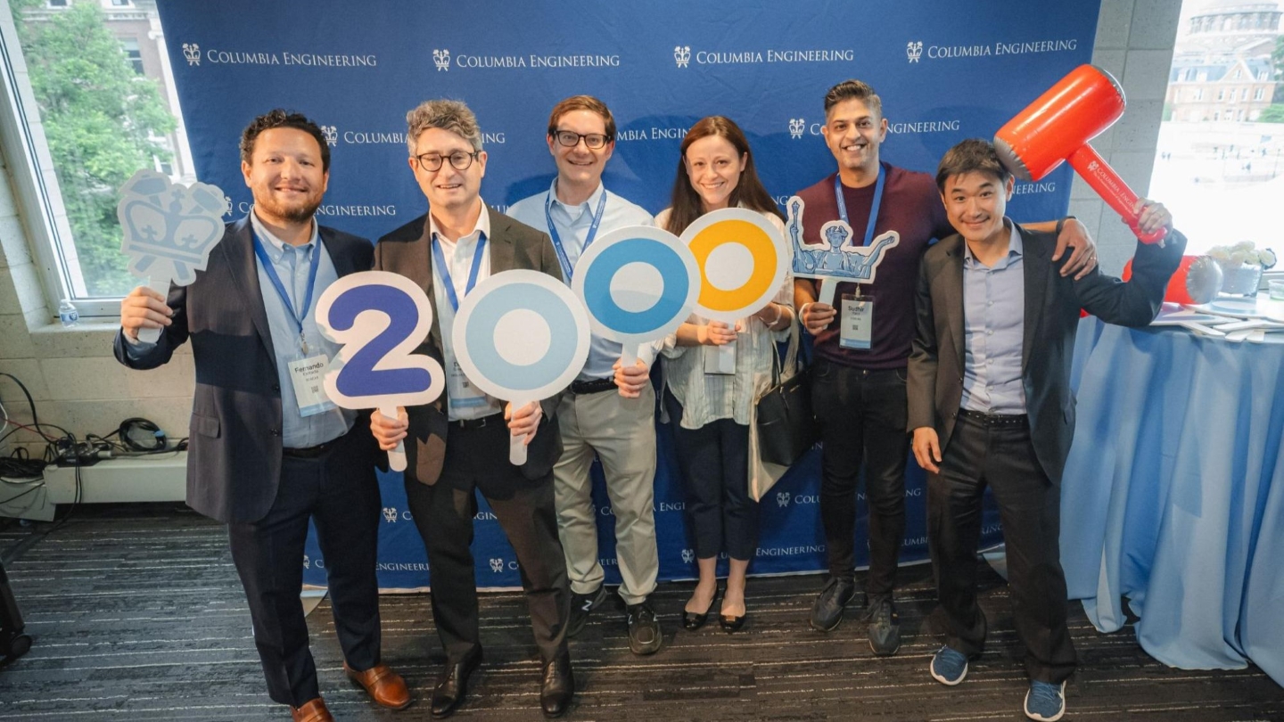 Five Columbia Engineering alums posing for a photo in front of a Columbia Engineering backdrop. Each of them holds up number signs to read "2000"