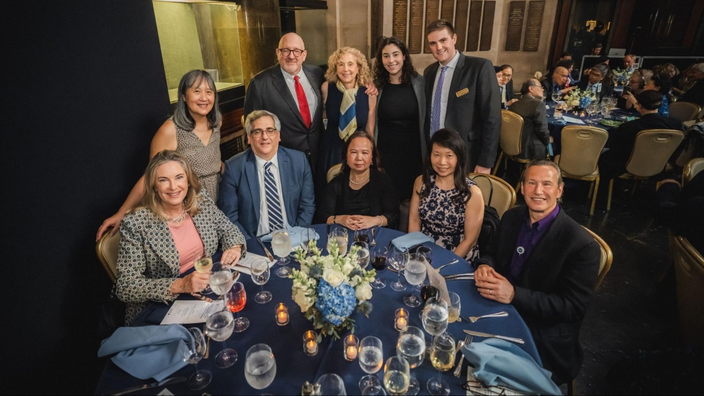 10 people posing for a photo at a dinner table adorned with flowers, candles, and drink glasses