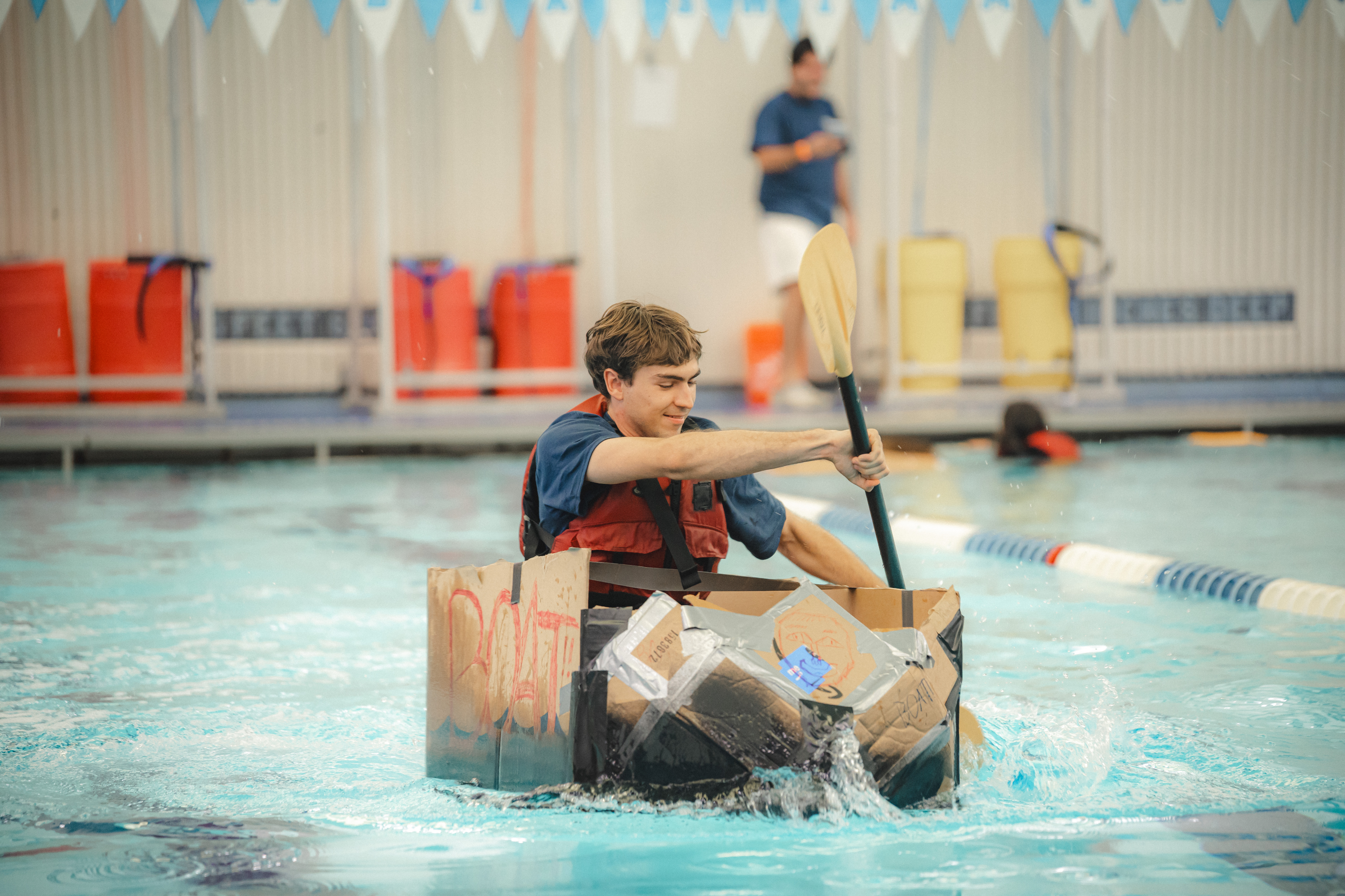 image of student rowing cardboard boat in pool