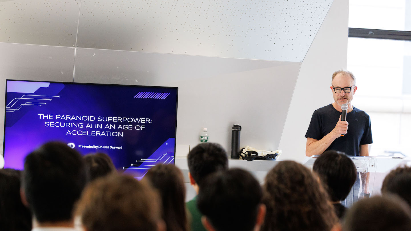 speaker standing next to screen reading "The Paranoid Superpower: Securing AI in An Age of Acceleration"