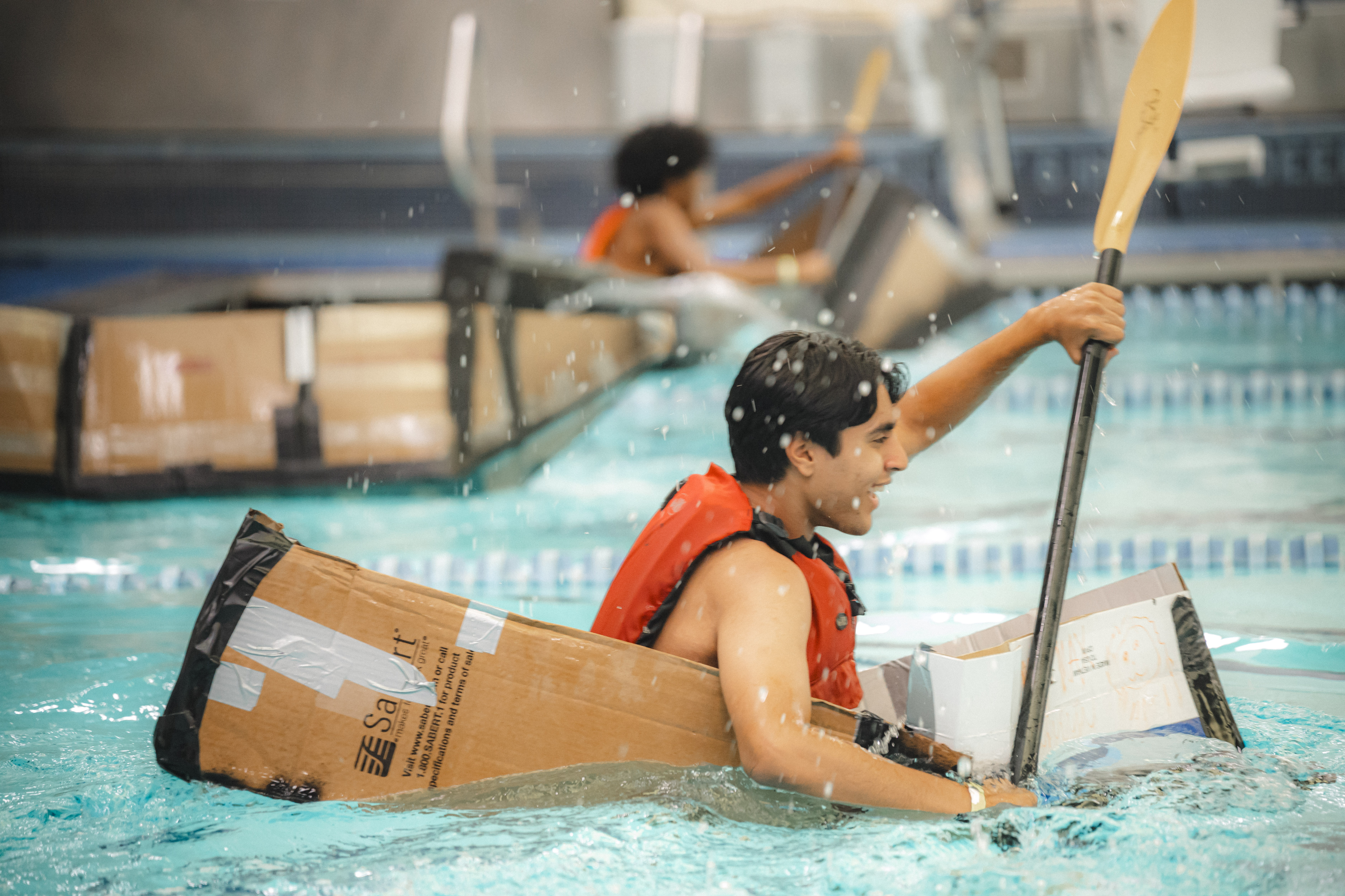 close up image of students rowing in cardboard boats on the pool