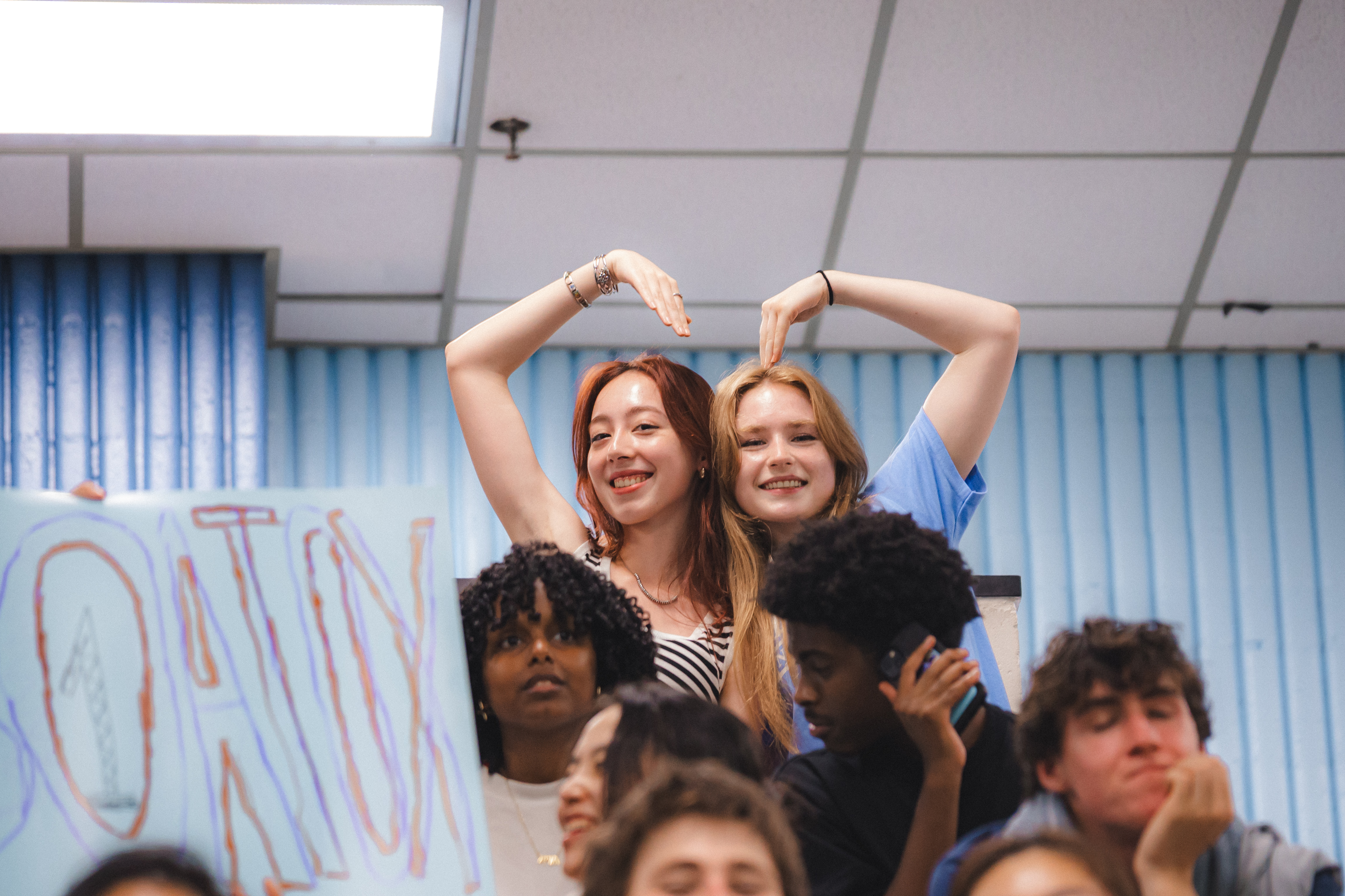 image of 2 students in the audience making a heart with their arms