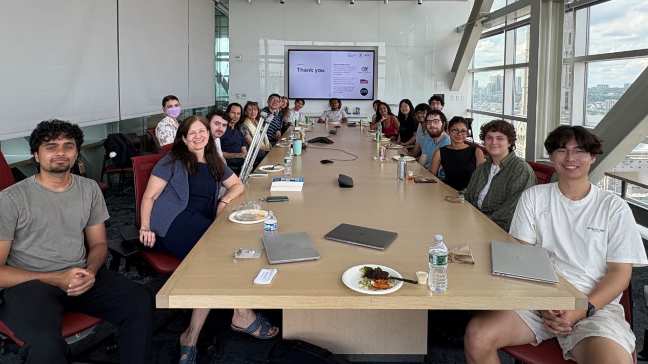 image of cyber nyc participants gathered at a large conference style table with ending slides of a powerpoint at the back