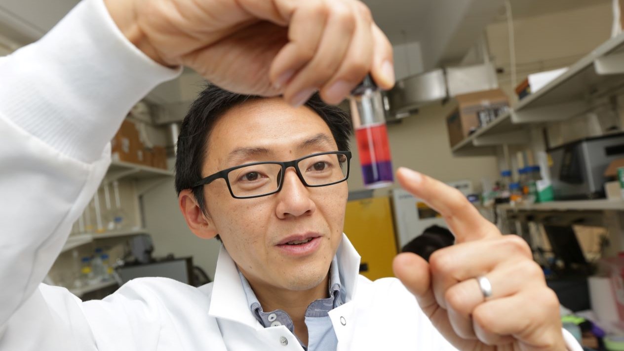 Ngai Yin Yip holding a lab vial up and pointing at it