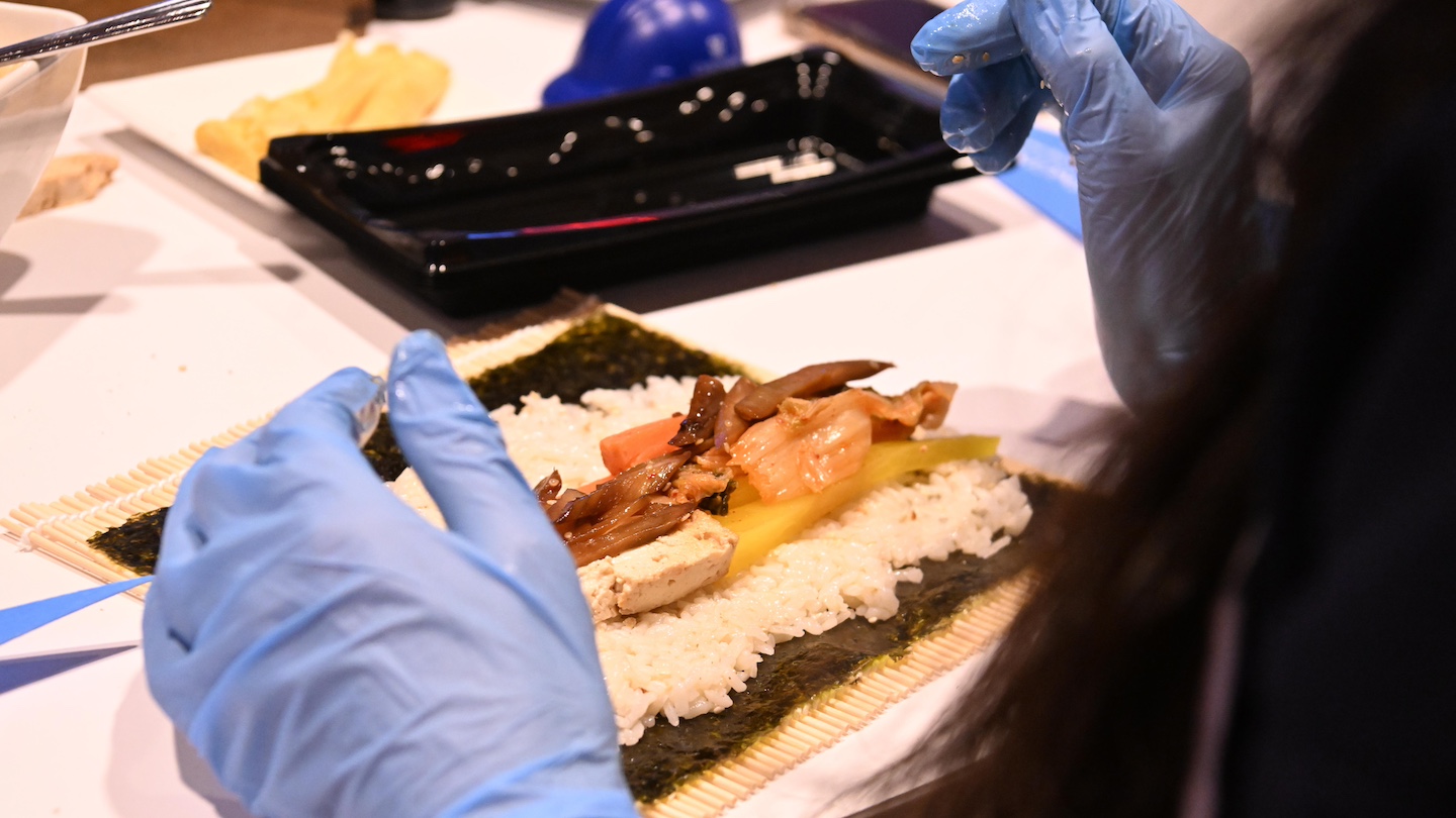 close up of kimbap about to be rolled, with person wearing light blue gloves