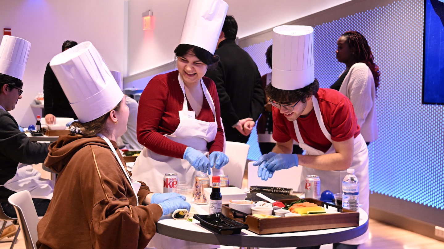 3 participants making kimbap together, wearing white chefs hats and aprons