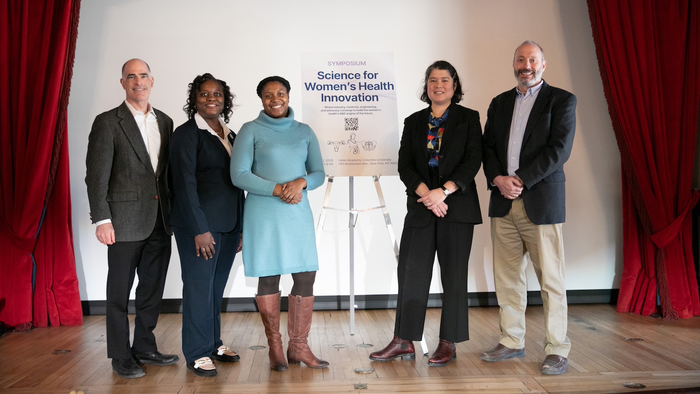Women's health symposium speakers and co-founders posed for a picture on stage, with a symposium banner in the middle