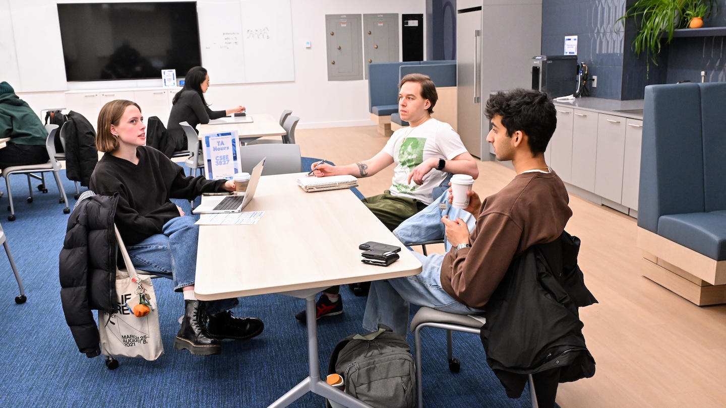 4 students seated together at table with laptops