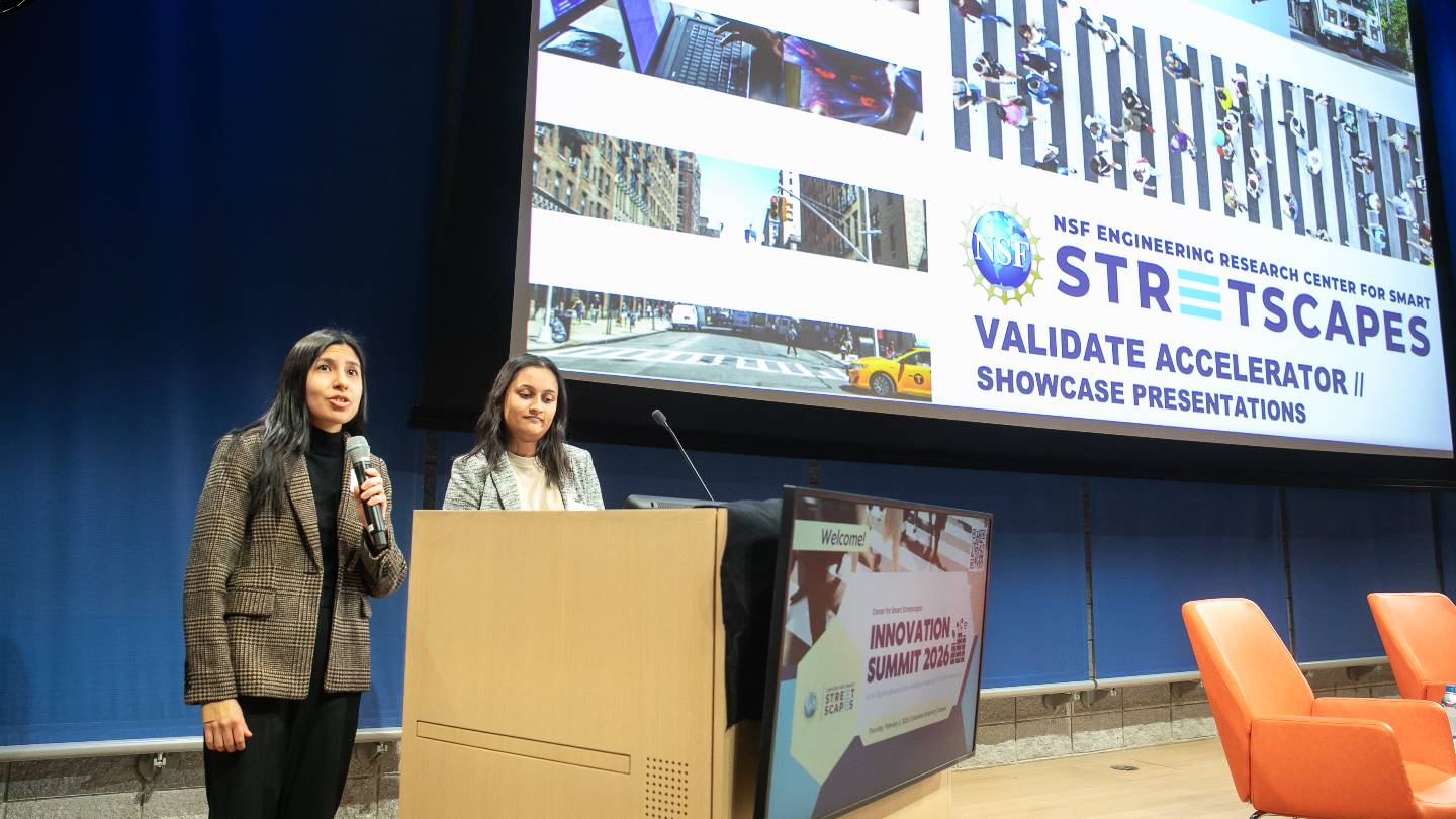 Two speakers standing behind a podium with a microphone. The sign in front of the podium reads "Welcome! Innovation Summit 2026". The projector screen on-stage reads "NSF Engineering Research Center for Smart Streetscapes. Validate Accelerator // Showcase Presentations"
