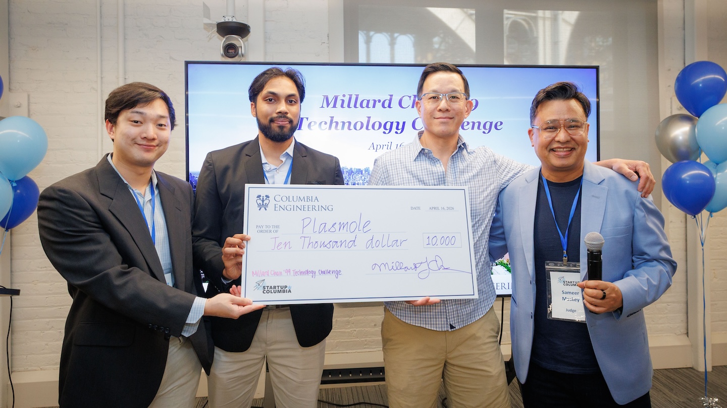 Four people pose in front of a “Millard Chan ’99 Technology Challenge” screen while holding a large $10,000 Columbia Engineering check; one person holds a microphone.