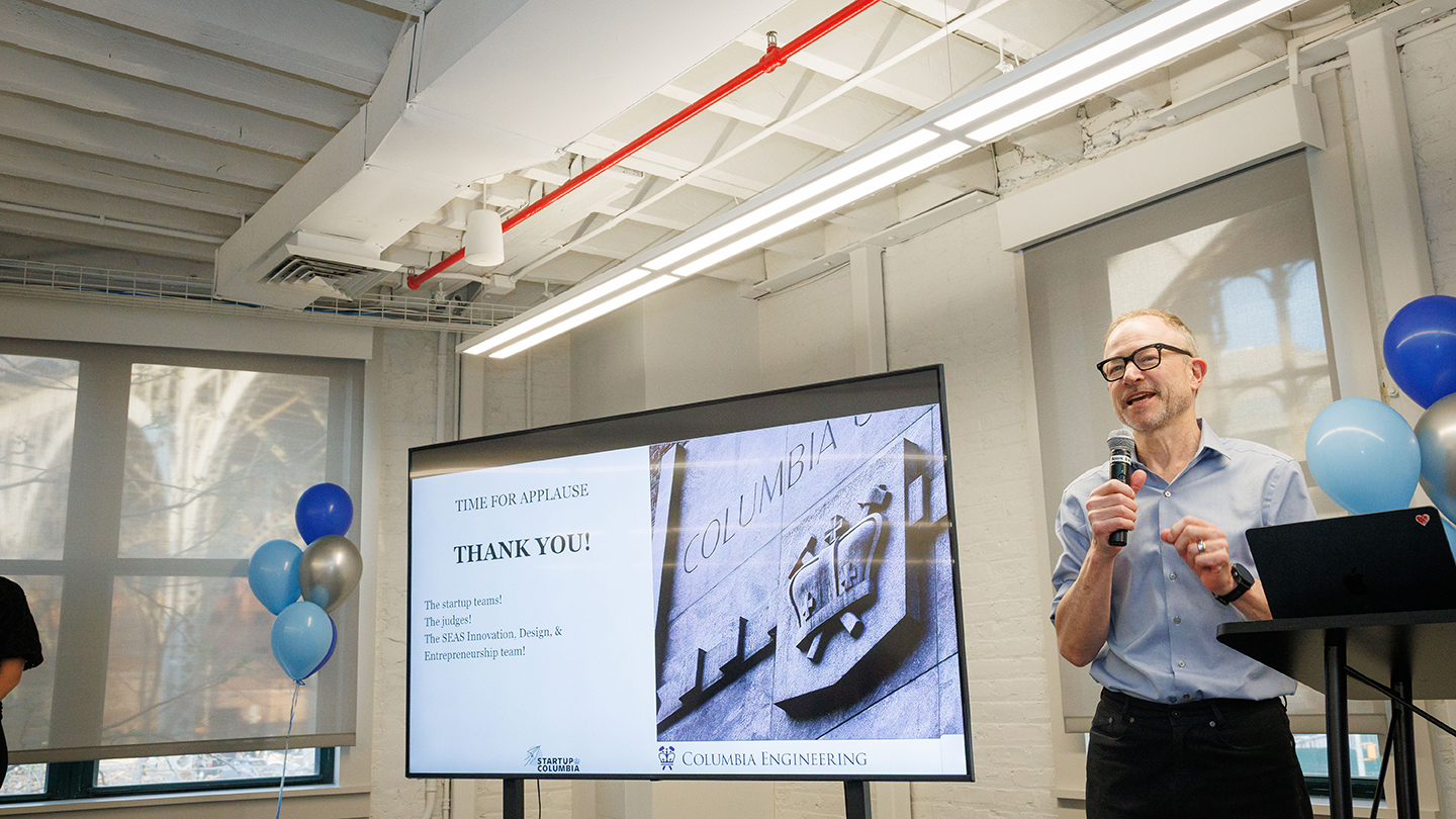 Presenter with a microphone stands beside a screen that says “Thank you” and displays the Columbia Engineering logo.