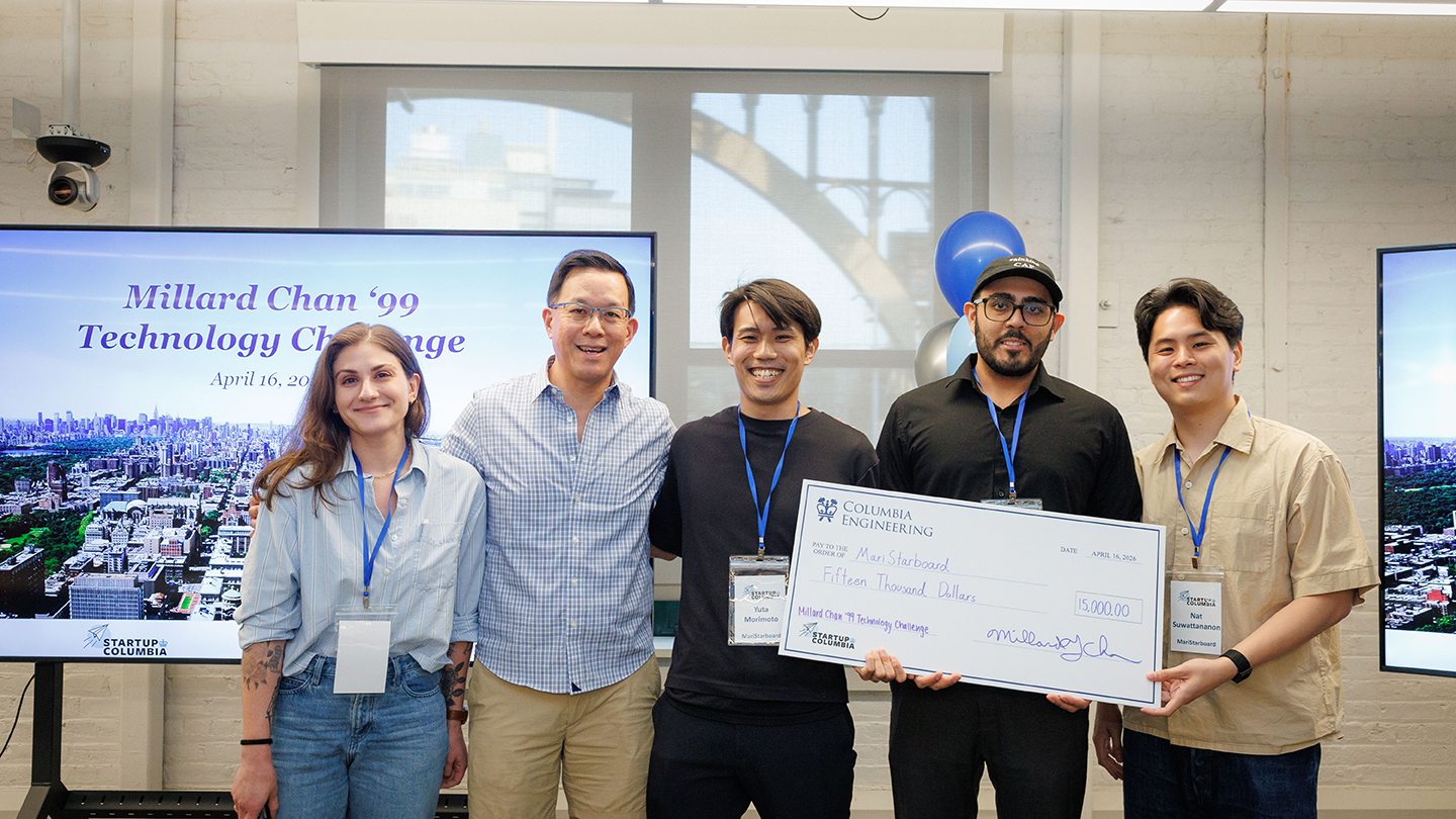 Four people pose in front of a “Millard Chan ’99 Technology Challenge” screen while holding a large $10,000 Columbia Engineering check; one person holds a microphone.