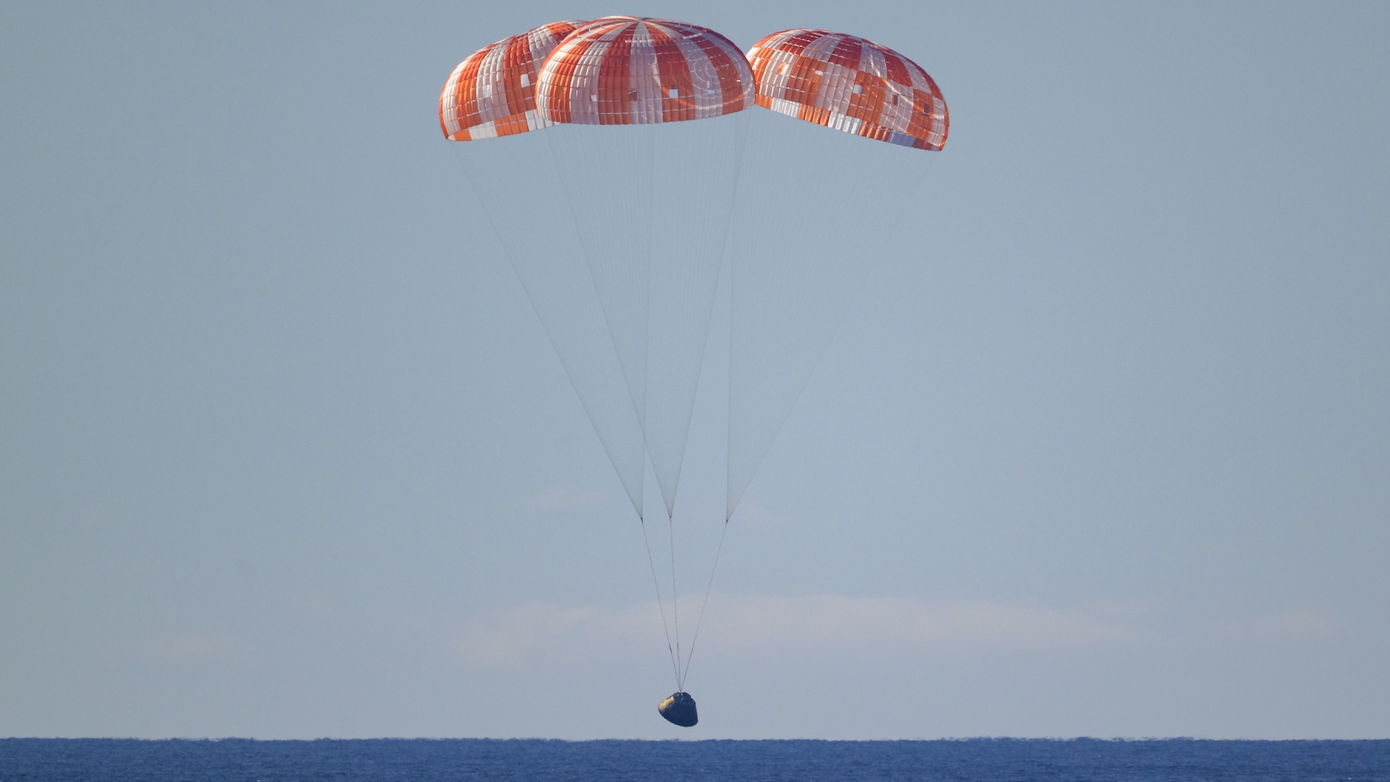 NASA’s Orion spacecraft with Artemis II crewmembers seen under parachutes as it lands in the Pacific Ocean off the coast of California, Friday, April 10, 2026. 