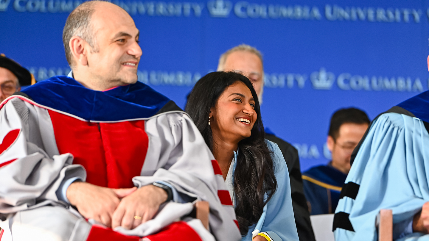 Divyadarshini Thirugnanasambandan seated onstage smiling during the ceremony, with the Columbia University backdrop behind.