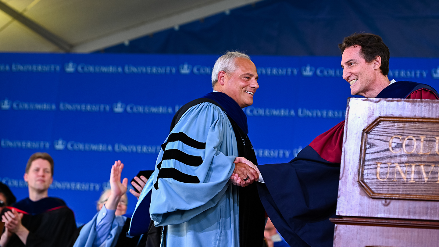 Thomas Caulfield and Barclay Morrison shake hands onstage beside a wooden podium during Columbia Engineering Class Day 2026.