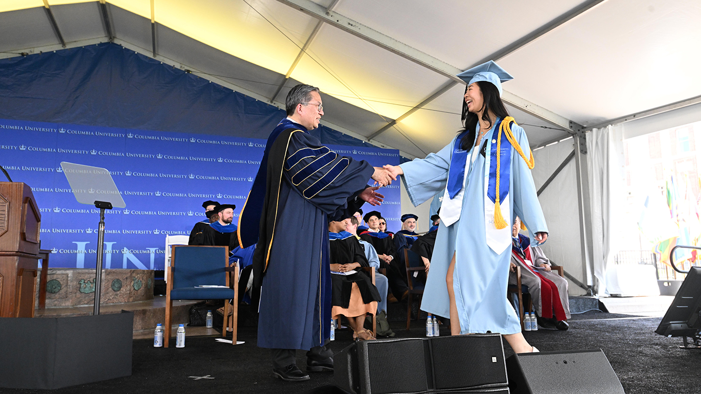 A Columbia Engineering student in graduation regalia shakes hands with Dean Shih-Fu Chang during 2026 Class Day ceremonies. Columbia Engineering faculty look on in the background.