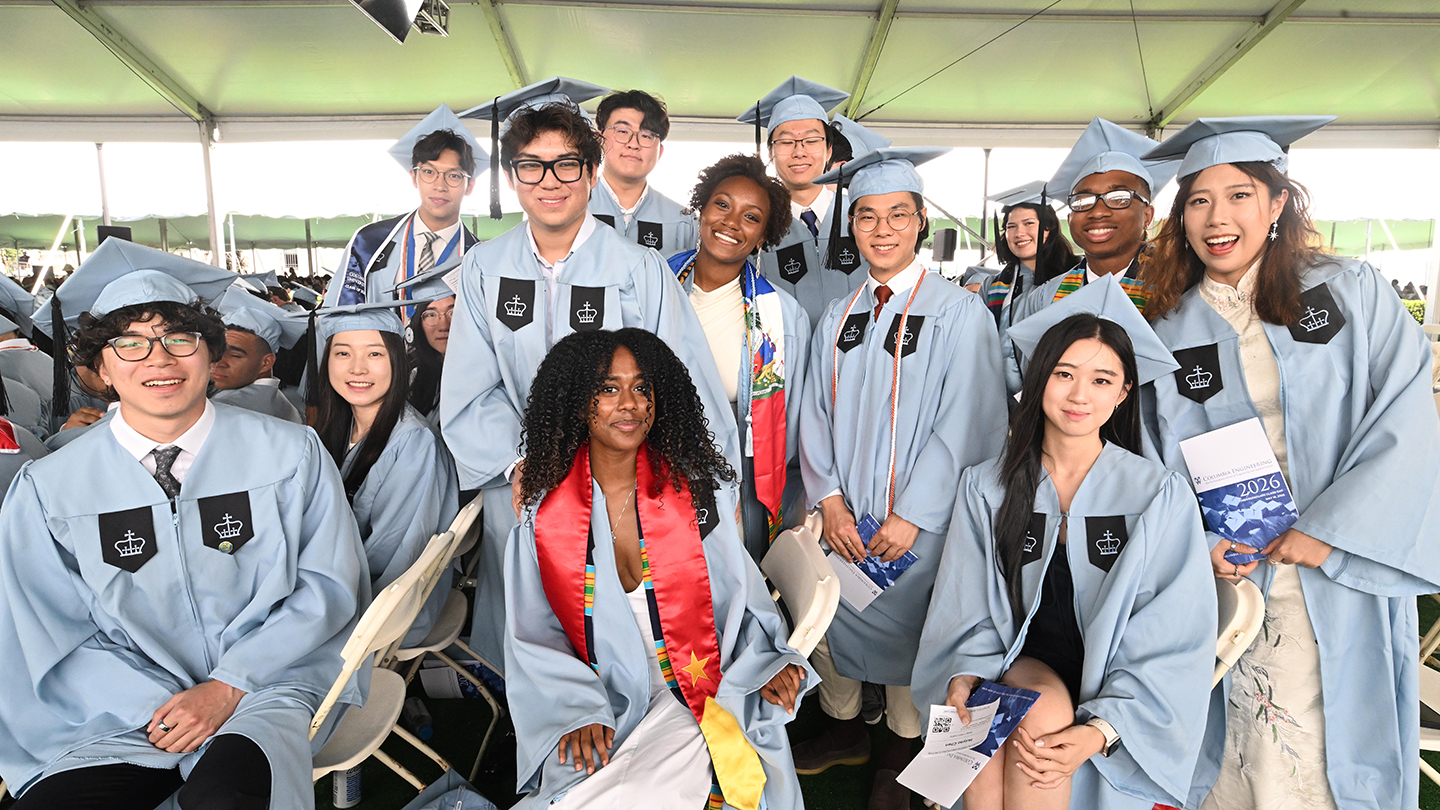 A group of Columbia Engineering students in graduation regalia posing for a photo under the ceremony tent