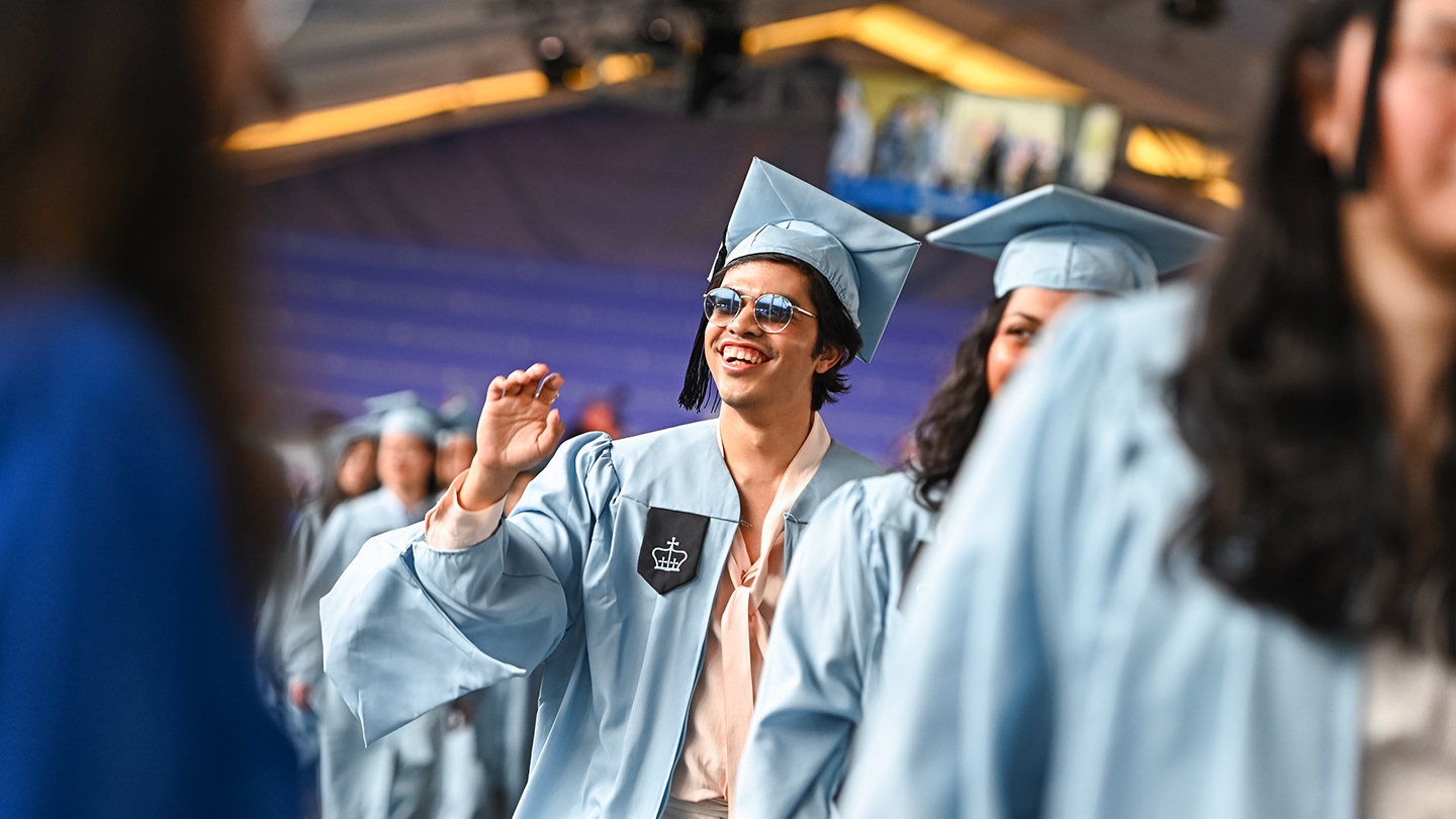 Columbia Engineering students in graduation regalia walk in a line under the ceremony tent.