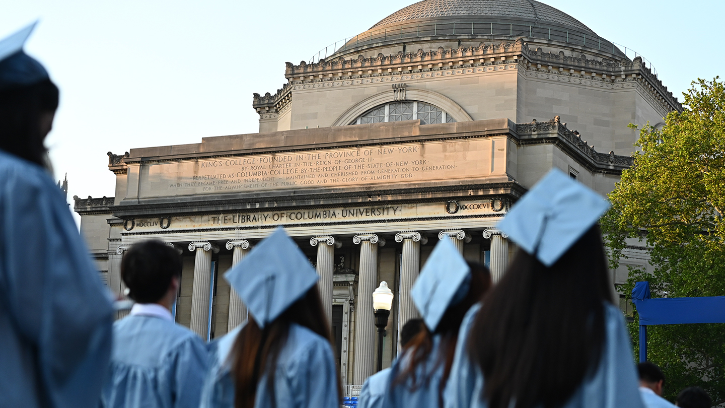 Columbia Engineering students in graduation regalia facing away from the camera in the foreground of Low Library