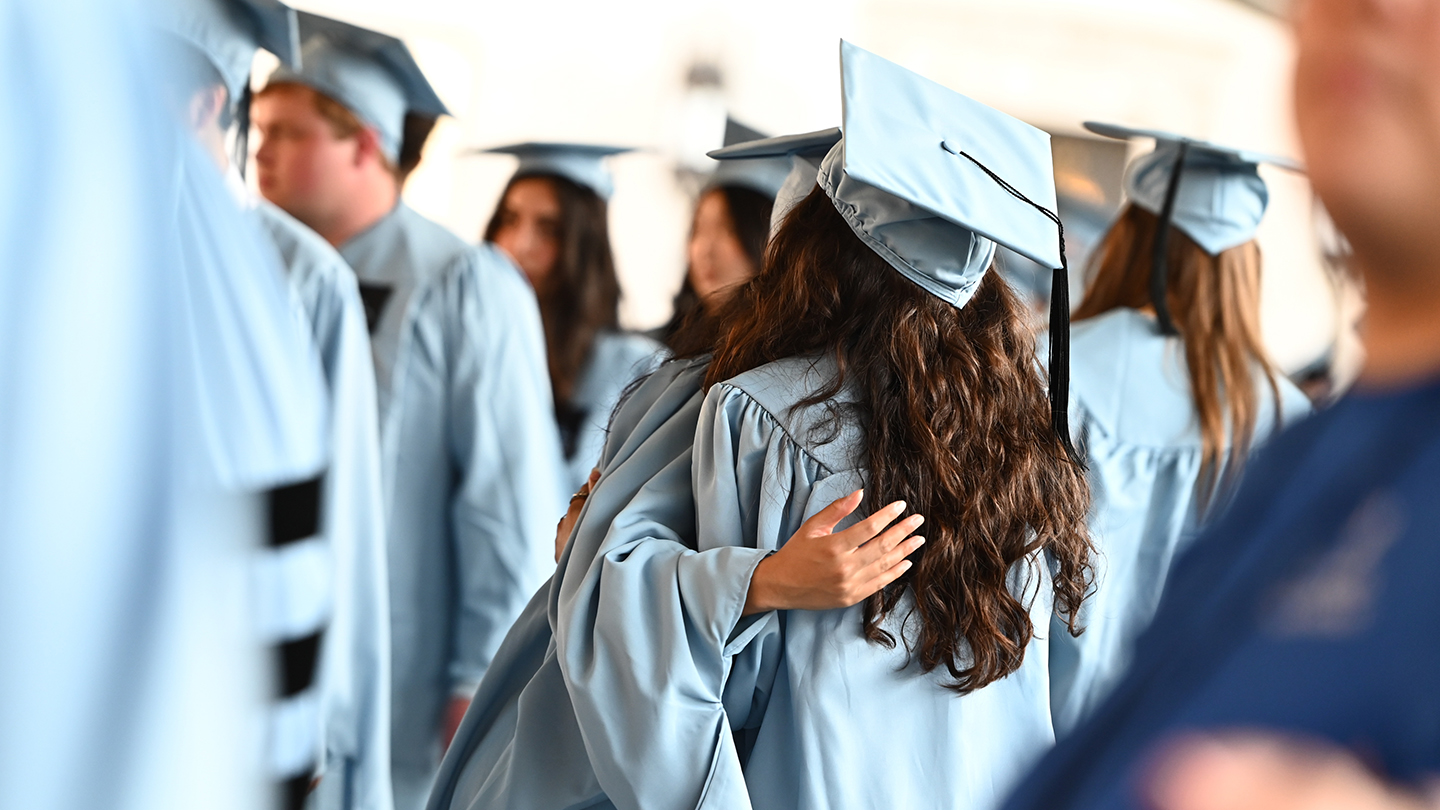 Columbia Engineering students in graduation regalia hugging among among a crowd of graduates.