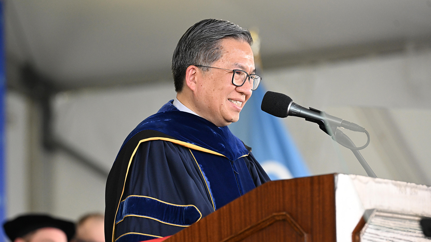 Columbia Engineering Dean Shih-Fu Chang in academic regalia smiles while speaking into a microphone at a podium onstage.