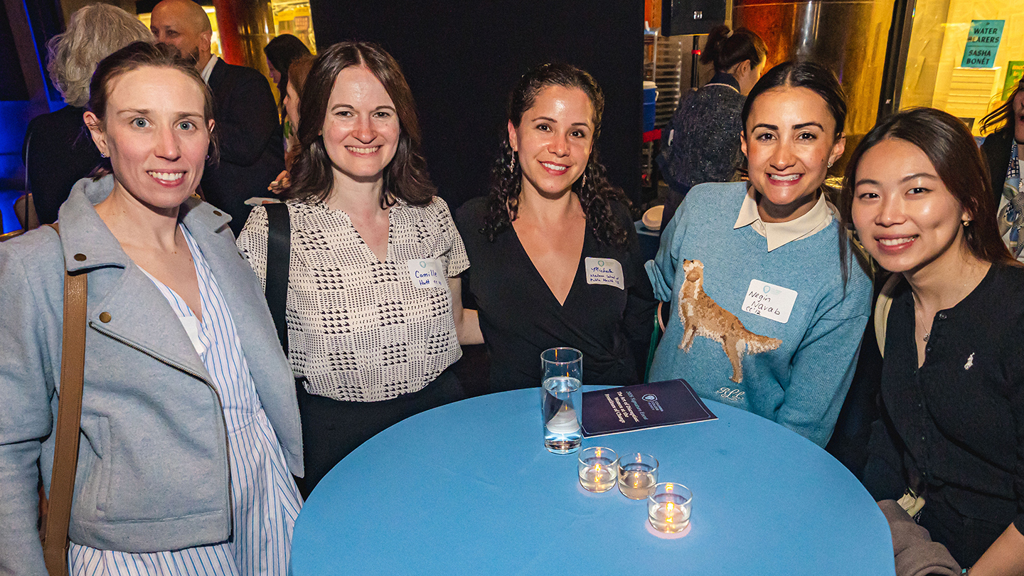 Five attendees pose smiling around a high-top table with candles at an indoor networking reception.