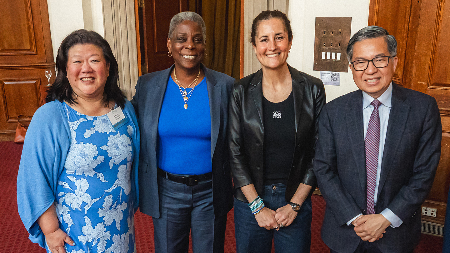 Group photo of four attendees standing close together and smiling in an indoor reception area.