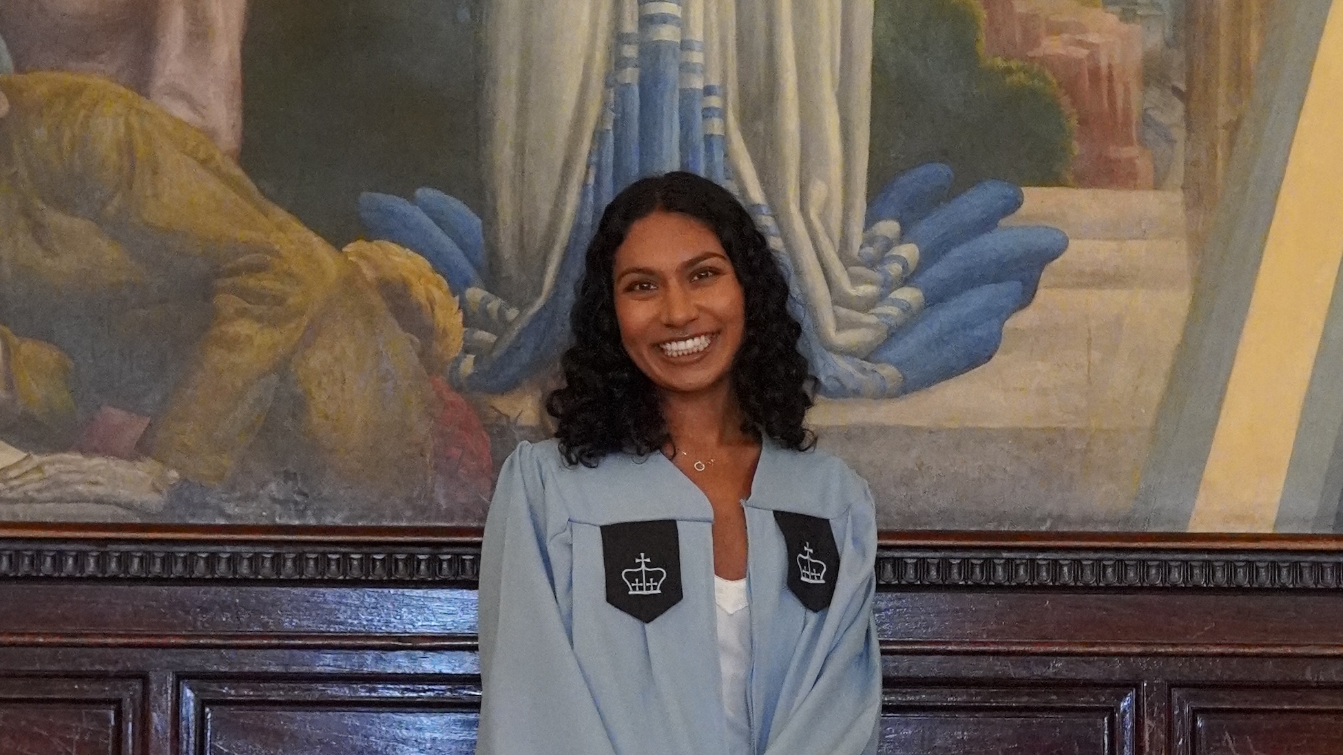 A woman wearing Columbia University graduation gown smiling for a photo