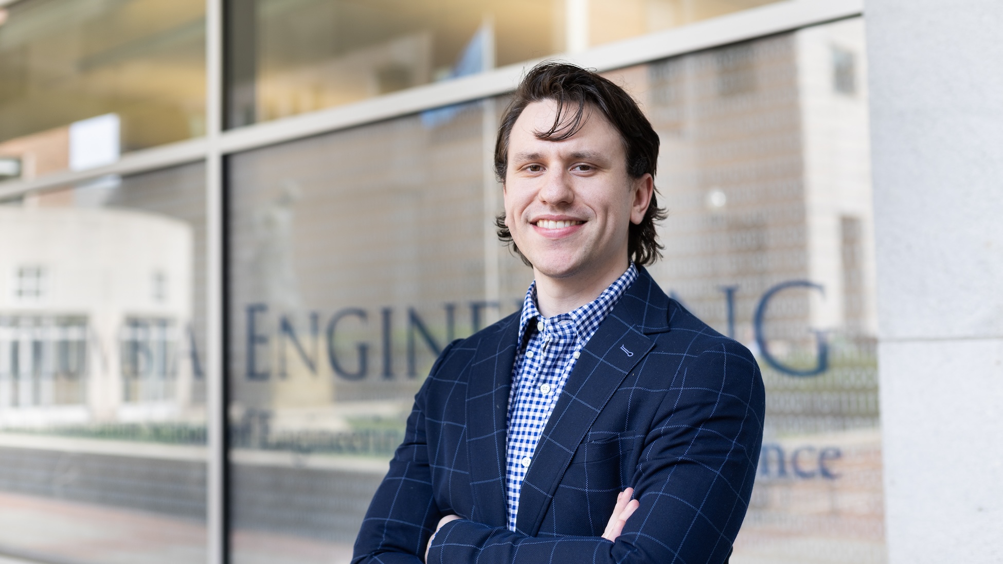 A man wearing a blazer smiling for a photo with his arms crossed. The glass behind him reads "Columbia Engineering" 